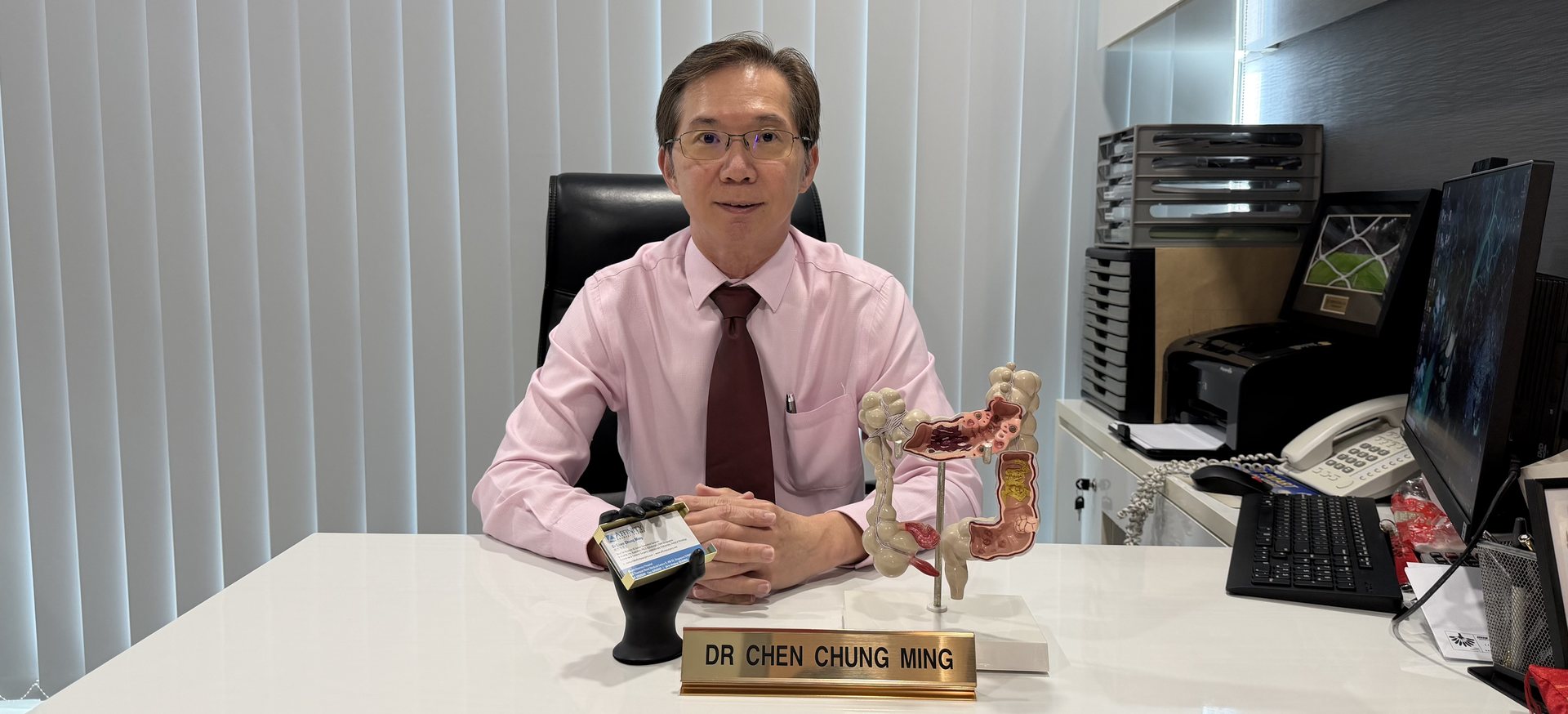 Dr Chen Chung Ming at his consultation desk with an anatomical model of the large bowel.